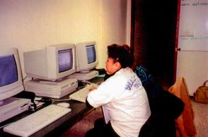 A woman sitting at a desk with three computers, working diligently on multiple tasks simultaneously.