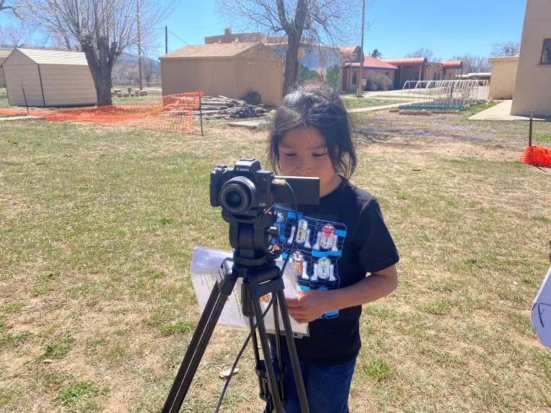 Girl Student at Taos Day School Outside Standing In Front of a Digital Camera on a Tripod Reading a Poem for the "I Am From Poem" Project.