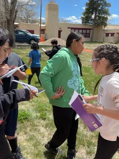 Boy and Girl Students at Taos Day School Holding Brochures and Talking About the Nature Scavenger Hunt.