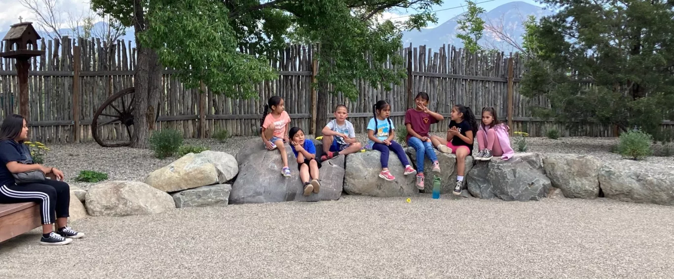 Taos Day School Boy and Girl Students in the CREATE Program Sitting Outside on Large Boulders.