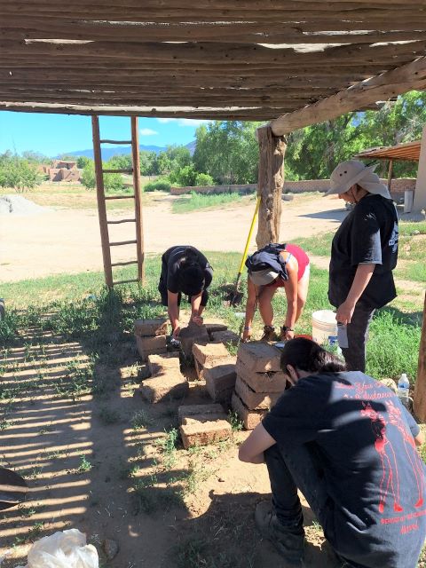 Four people working with mud blocks outside.