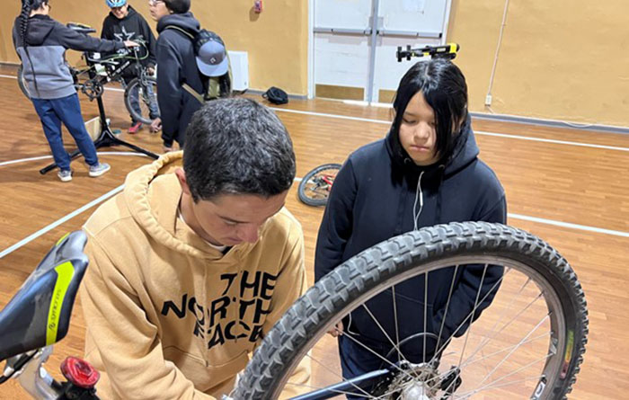 Students working on bicycle in school gymnasium.
