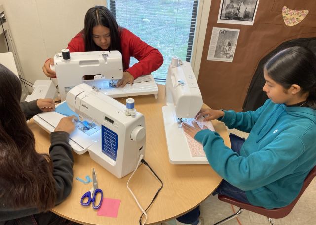 Eighth grade students learning how to use sewing machines.