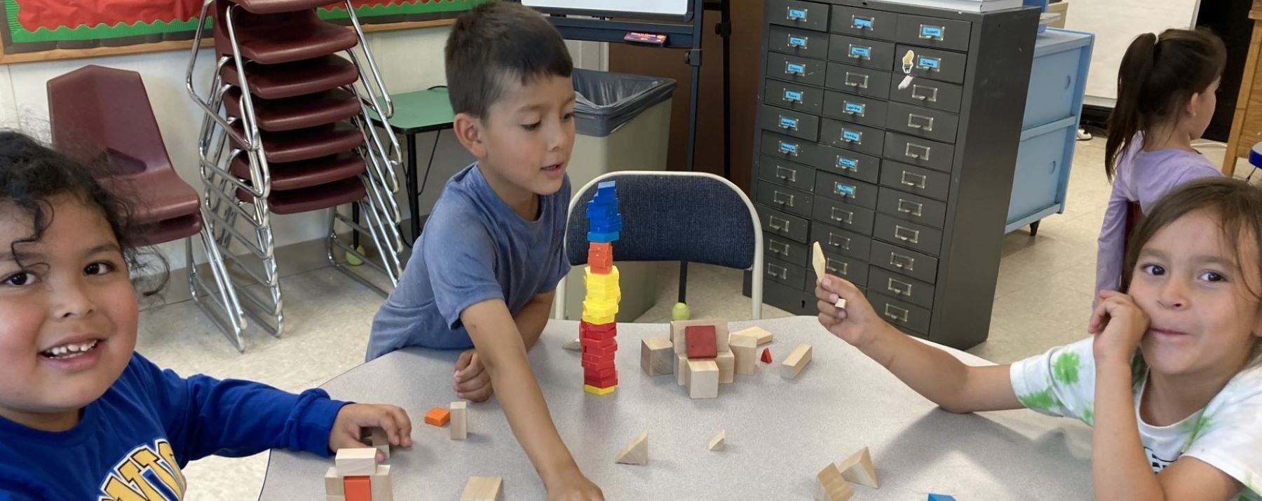 Three first grade students building with colorful blocks at a table.