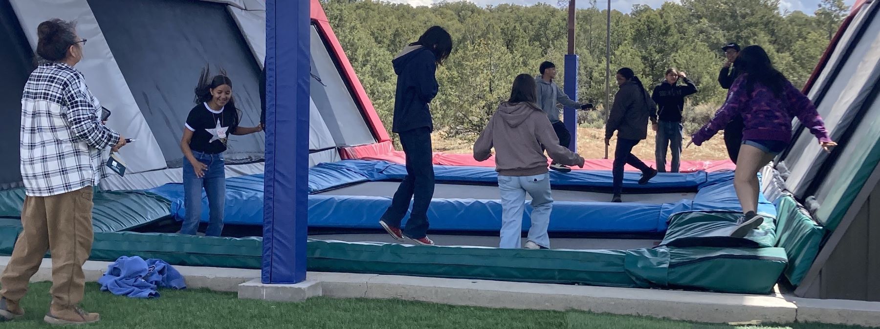 A group of students joyfully bouncing together on a trampoline in a sunny outdoor setting.