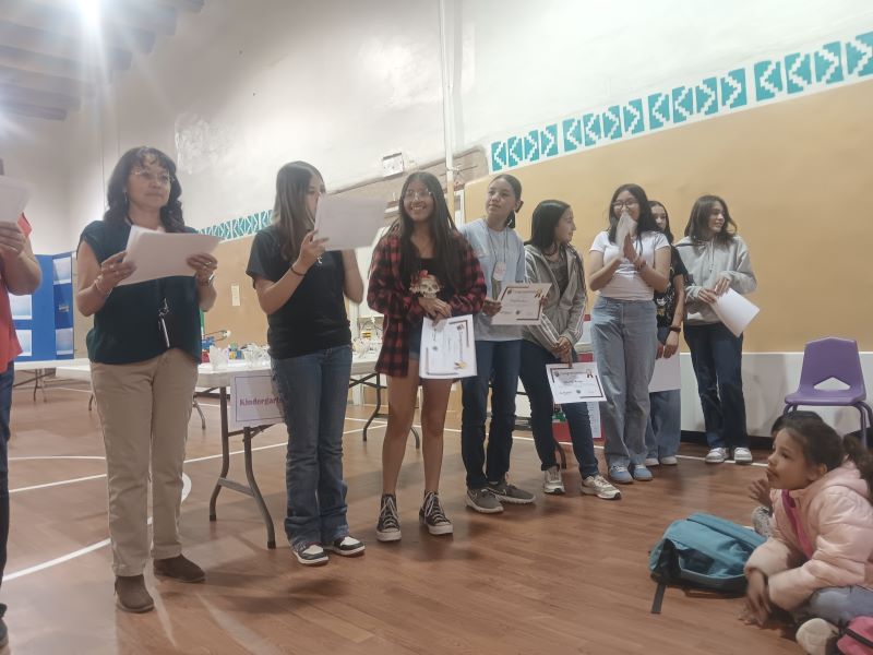 Several students standing together in a gymnasium, holding their award certificates.
