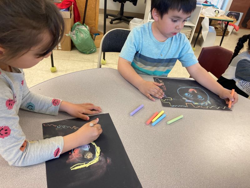 Students using chalk on black paper to create their self portraits.
