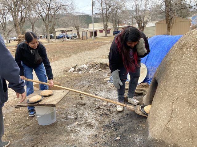 Students putting bread into horno using a very long handled paddle.