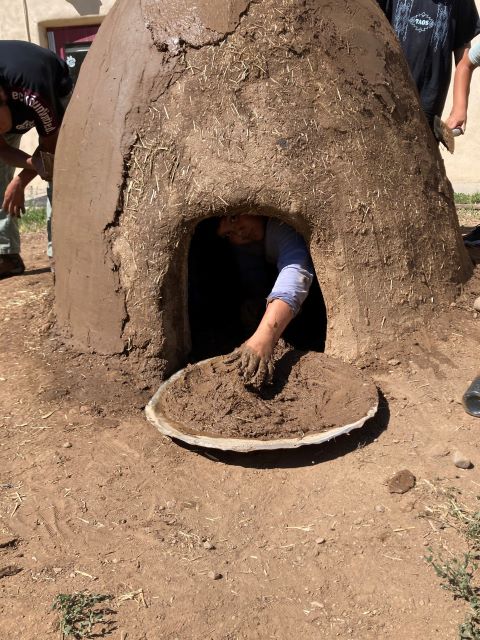 Child's hand reaching out of a horno to grab mud for the inside.