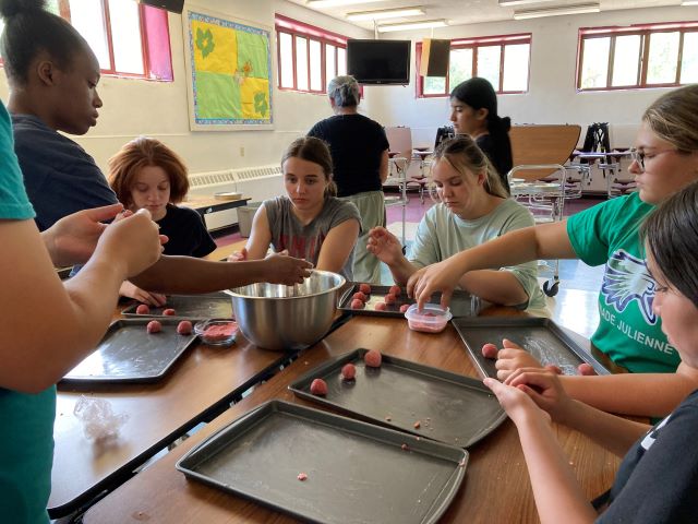 Group of students sitting together at table preparing meatballs and placing on cookie sheets.