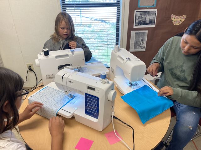Group of three students at a round table with sewing machines.