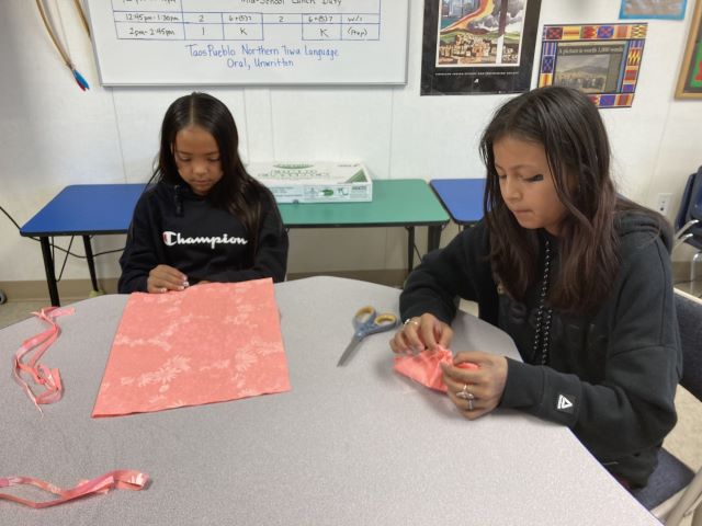 Two students sitting together at a table and hand-sewing fabric pieces.