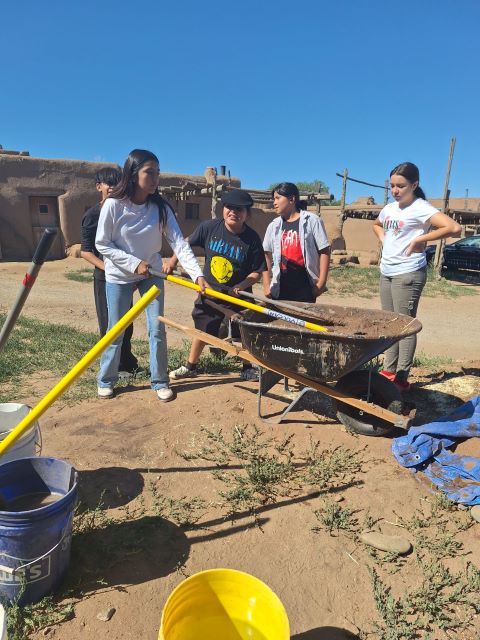 Group of students working with mud and tools in a wheelbarrow outside.