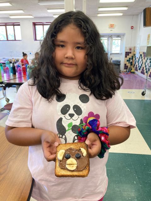 Student holding bread with bananas, blueberries and hazelnut spread in the shape of an animal.