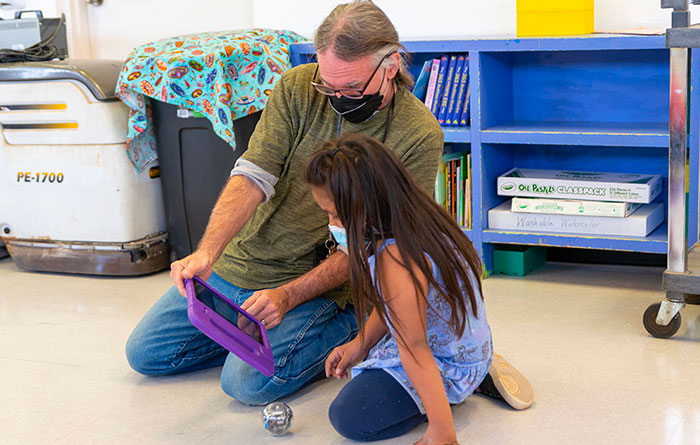 Teacher helping a student use a tablet.