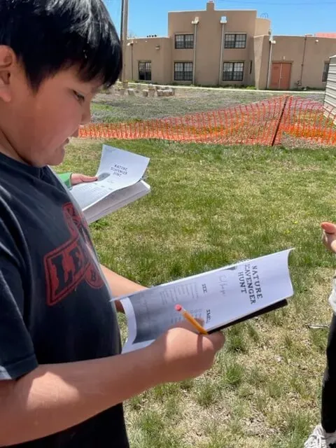 A Boy Student at Taos Day School Reading a Brochure on the Nature Scavenger Hunt.