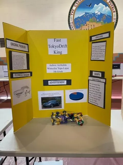 "Fast Tokyo Drift King" Trifold Project Board and Science Project Displayed on a Table Inside the Gym at Taos Day School.
