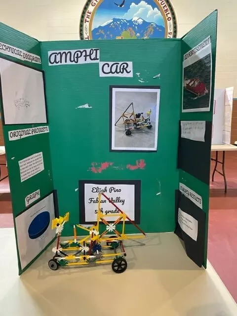 "Amphi Car" Trifold Project Board and Science Project Displayed on a Table Inside the Gym at Taos Day School.